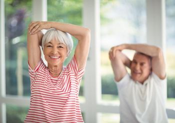 uśmiechnięty starszy mężczyzna i uśmiechnięta starasza kobieta ćwiczą mięśnie w domu
