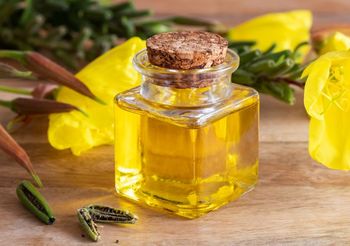 Buteleczka z olejem z wisiołka w otoczeniu zóltych kwiatów wiesiołka